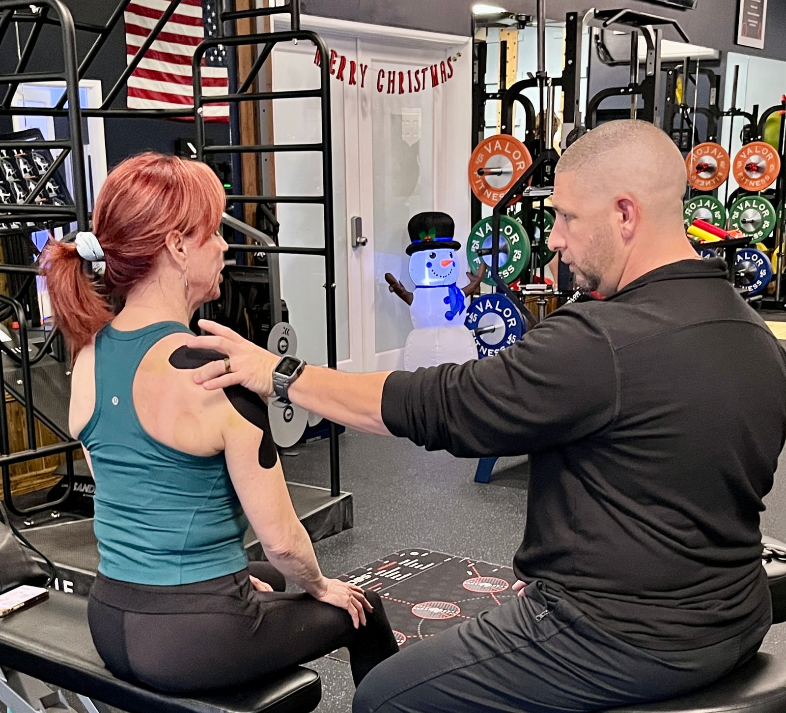 Seated physical therapist assessing a patient's upper back and shoulder, with kinesiology tape on her shoulder, at Improved Motions in Stuart, FL