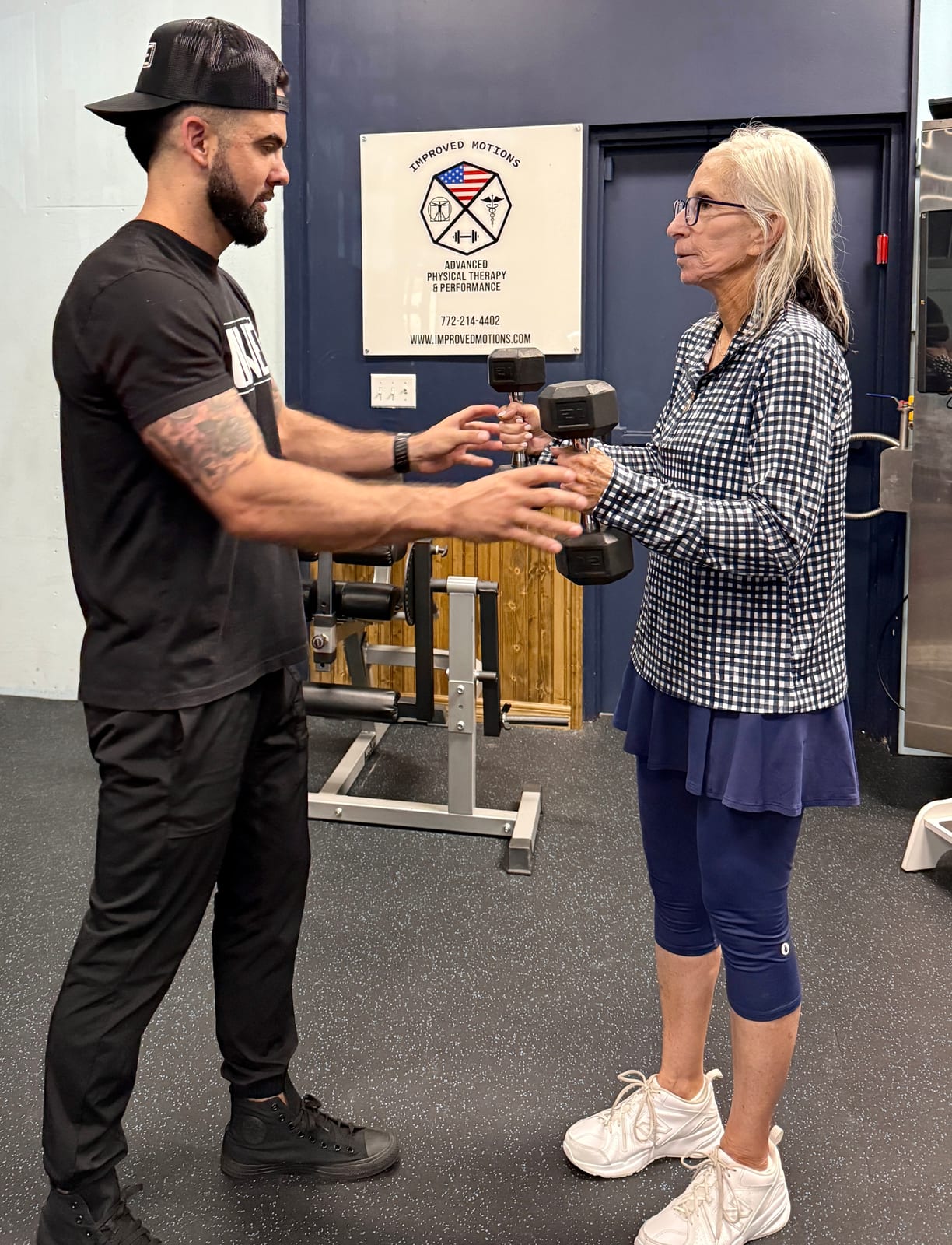 Physical therapist handing dumbbells to an older woman for a standing strength exercise at Improved Motions in Stuart, FL